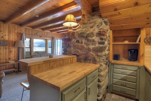 Interno accogliente di una baita rustica con parete in pietra, mobili in legno e vista da una finestra.
