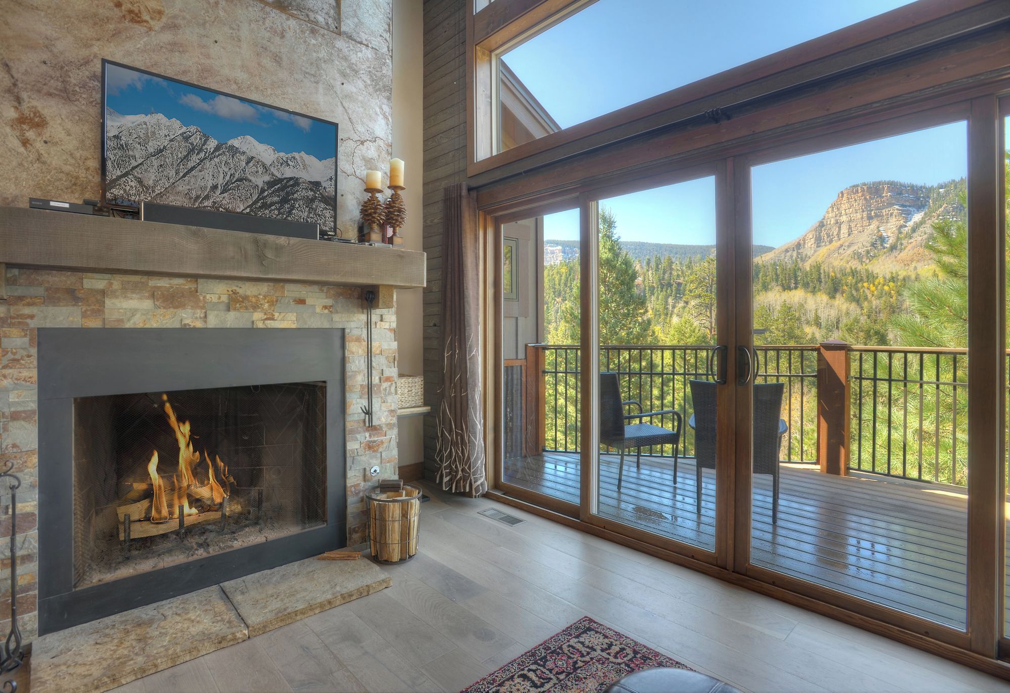 A spacious living room with a fireplace, large windows, and a deck with outdoor furniture.