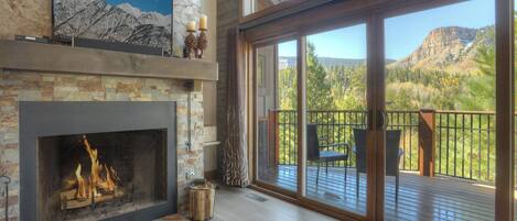 A spacious living room with a fireplace, large windows, and a deck with outdoor furniture.