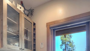 Een keuken met een houten kastje, een vitrineplank en uitzicht op een bergachtig landschap door een schuifdeur.