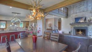 Een ruime woonkamer met een open haard, een eethoek met een grote houten tafel, en een keuken met moderne apparatuur.