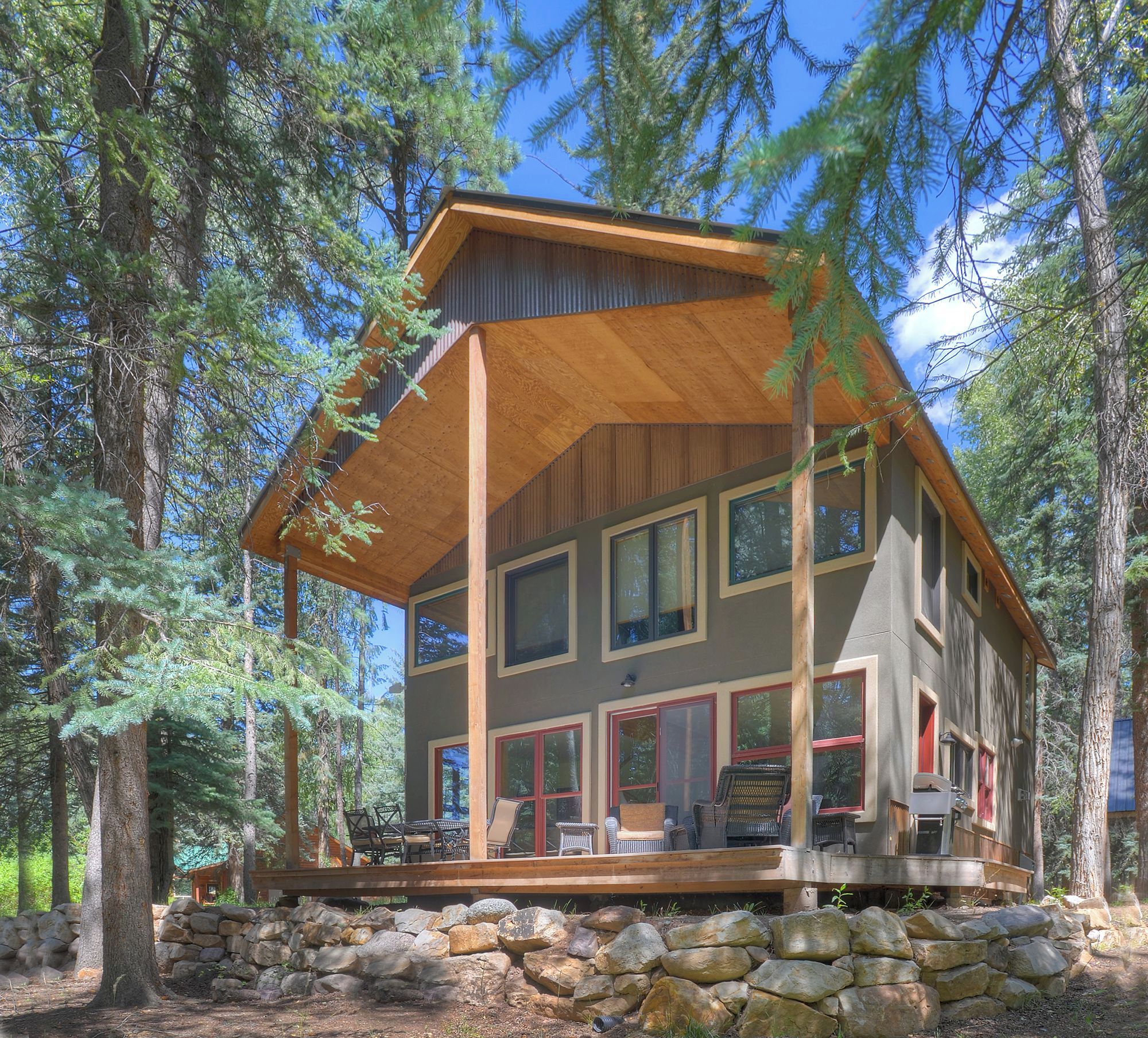 A two-story cabin with a wooden deck, large windows, and a stone foundation.
