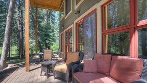 A covered deck with wicker furniture, large windows, and a view of the forest. - Creekside Retreat - Waterfront Home 20 Minutes from Downtown Durango (Durango)