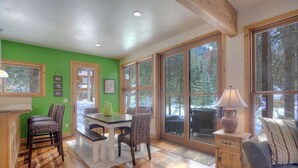 A cozy room with a green wall, wooden floor, and large windows offering a view of trees. - Creekside Retreat - Waterfront Home 20 Minutes from Downtown Durango (Durango)