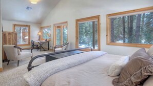 A bedroom with a large bed, a desk, and two chairs. There are multiple windows providing views of a forest. - Creekside Retreat - Waterfront Home 20 Minutes from Downtown Durango (Durango)