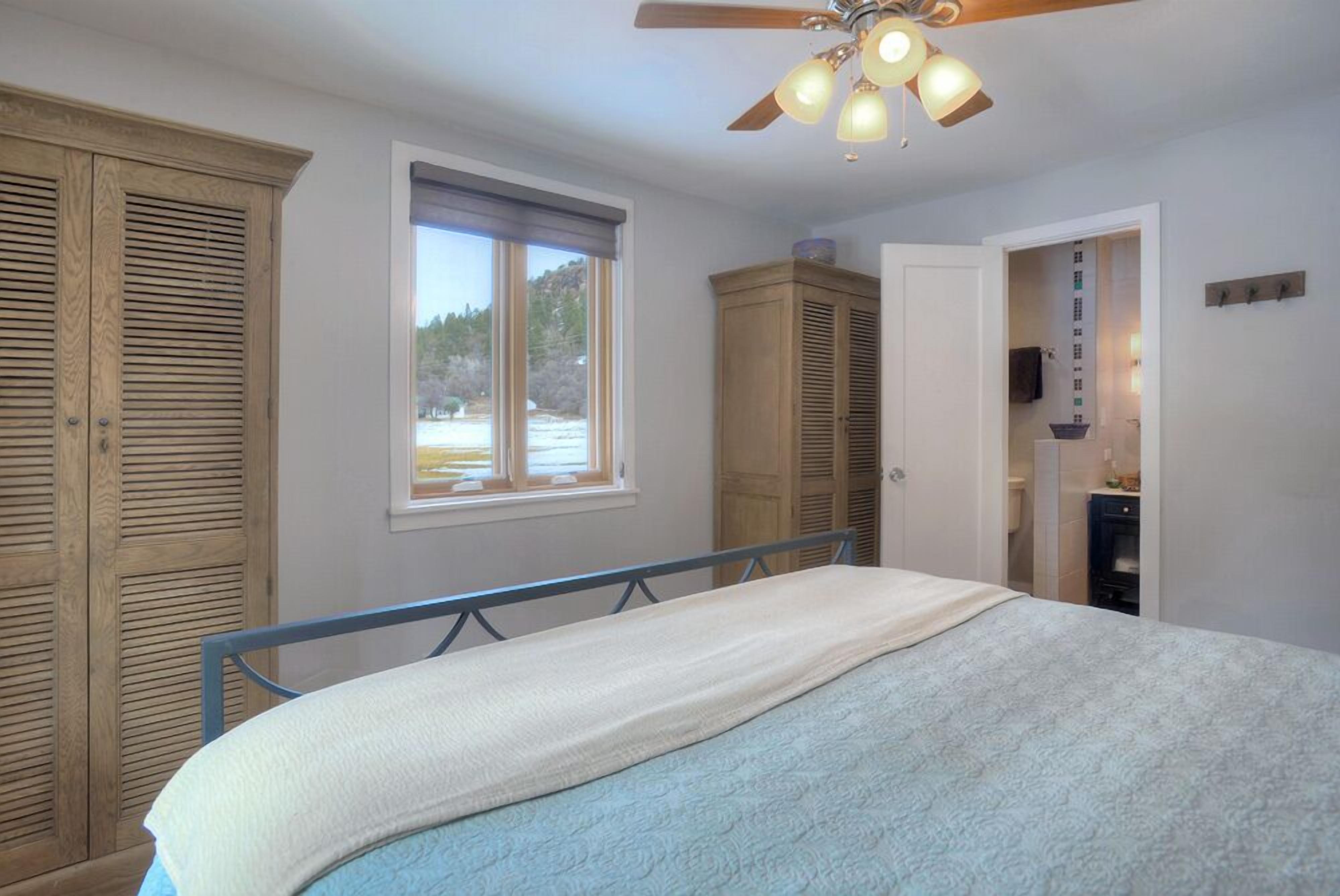 Ein Schlafzimmer mit Bett, Deckenventilator, Fenster und Holzschränken.