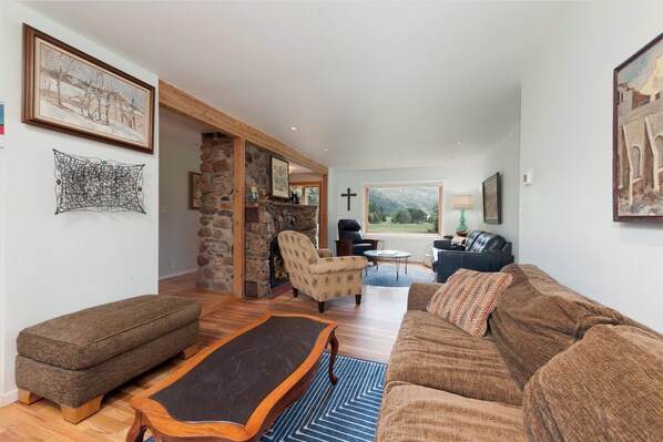 A cozy living room with a stone fireplace, a large window with a view of the outdoors, and a comfortable seating area with a sofa and armchairs.