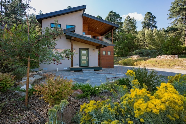 A modern two-story house with a green door, a balcony, and a stone wall in the background.