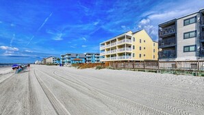 A beachfront hotel with multiple balconies, a sandy beach in the foreground, and a clear blue sky. - Afterdeck 104 - Two Bedroom, Two Bath Oceanfront Condo (Garden City Beach)
