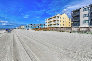A beachfront hotel with multiple balconies, a sandy beach in the foreground, and a clear blue sky.
