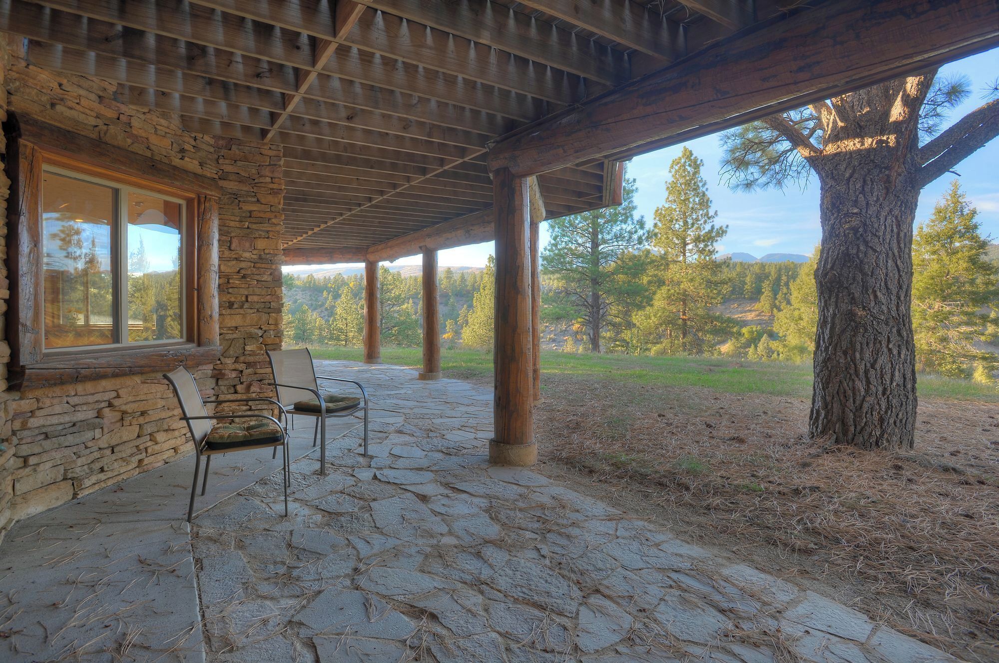 A covered patio with stone flooring, a stone wall, and a view of a forested landscape.