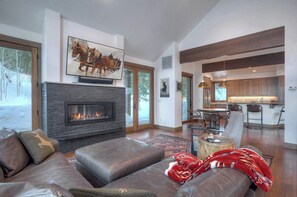 Uma sala de estar moderna com lareira, sofá de couro e área de jantar com banquetas.