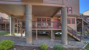A multi-story building with a covered outdoor area supported by concrete columns, featuring a wooden deck with railings and a red door. - Mesa Haven | Downtown Durango Access, Pool/Hot Tub, Near FLC and Golf (Durango)