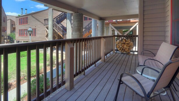 A covered outdoor deck with a wooden railing, a stack of firewood, and two chairs. - Mesa Haven | Downtown Durango Access, Pool/Hot Tub, Near FLC and Golf (Durango)
