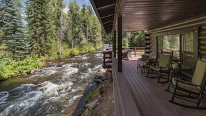 A wooden deck with outdoor seating overlooking a flowing river, surrounded by dense forest.