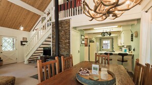 A spacious living room with a large wooden dining table, a fireplace, and a staircase leading to an upper level.