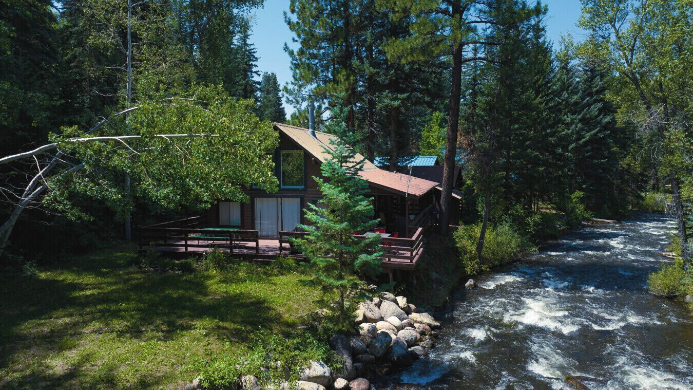 Une cabane au bord d’une rivière, dotée d’une terrasse et d’un petit porche.