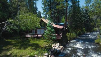 Une cabane au bord d’une rivière, dotée d’une terrasse et d’un petit porche.