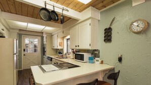 A compact kitchen with white cabinetry, a microwave, a sink, and a bar area with stools.