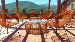Une terrasse dotée de meubles en osier et offrant une vue sur des montagnes verdoyantes.