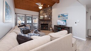 A living room with a stone fireplace, a large sofa, a television, and a ceiling fan.