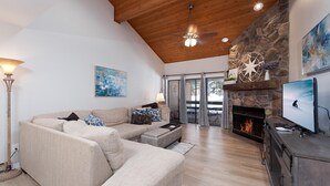 A spacious living room with a high ceiling, a stone fireplace, a television, and a large window.