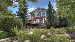 A two-story house with a wooden exterior, a balcony with flower boxes, and a stone pathway leading to the entrance.