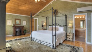 A spacious bedroom with a four-poster bed, a wooden ceiling, and a fireplace.