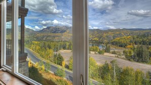 Vista desde una ventana sobre un paisaje montañoso con follaje otoñal, una carretera y un lago.