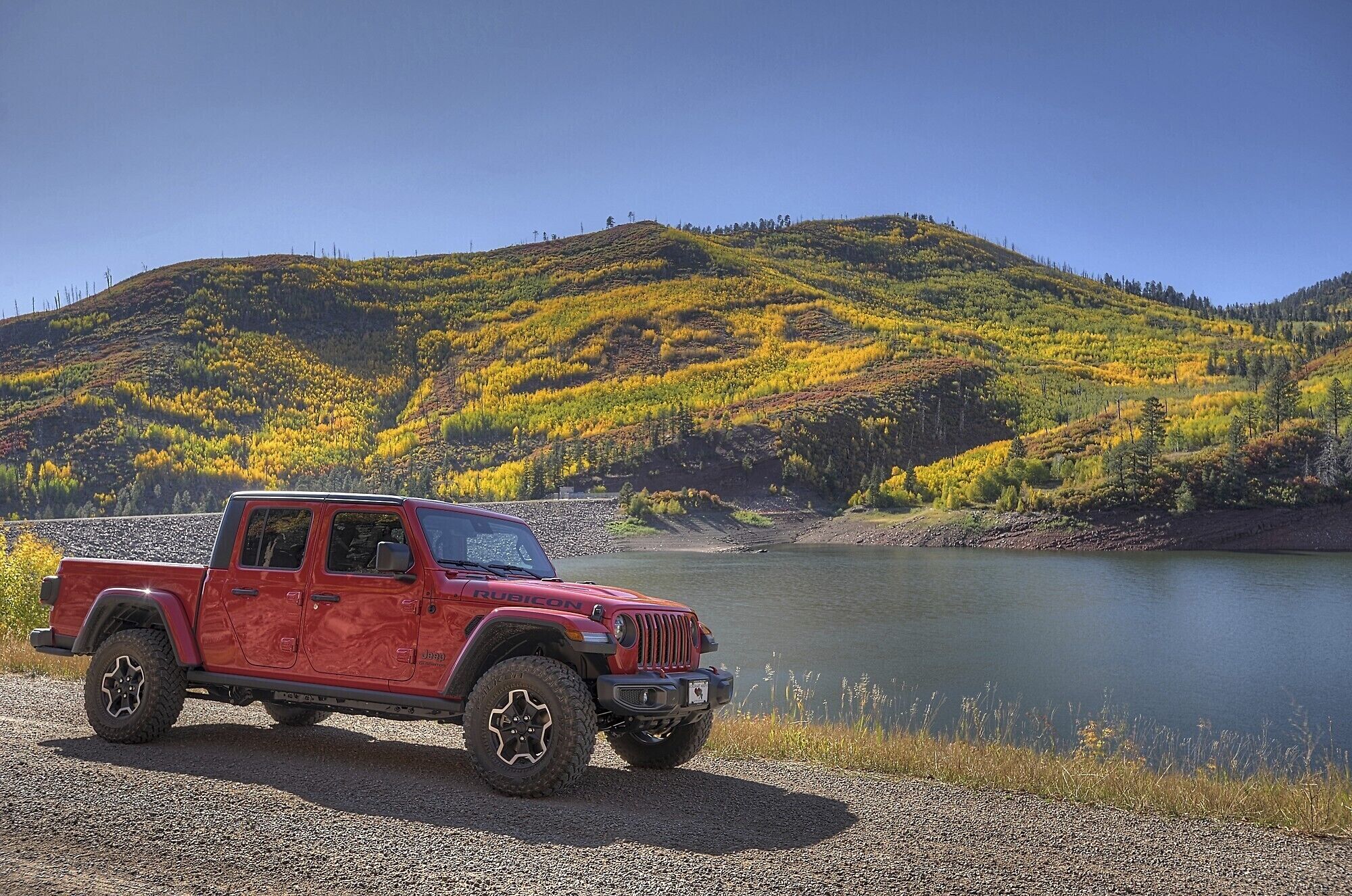 Un véhicule tout-terrain rouge est garé au bord d’un lac, avec un paysage vallonné en arrière-plan.