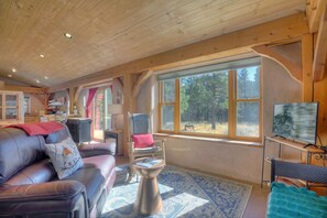 A cozy cabin interior with a leather sofa, a metal coffee table, and a large window offering a view of the forest. - Solar-Powered Cabin | Starlink, Secluded Retreat (Durango)