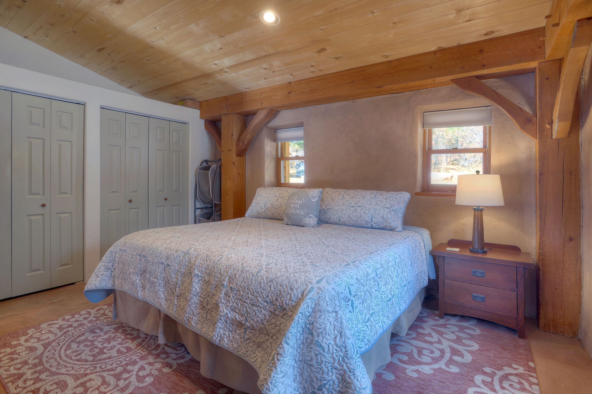 A bedroom with a bed, a nightstand, a lamp, a window, and a wardrobe.
