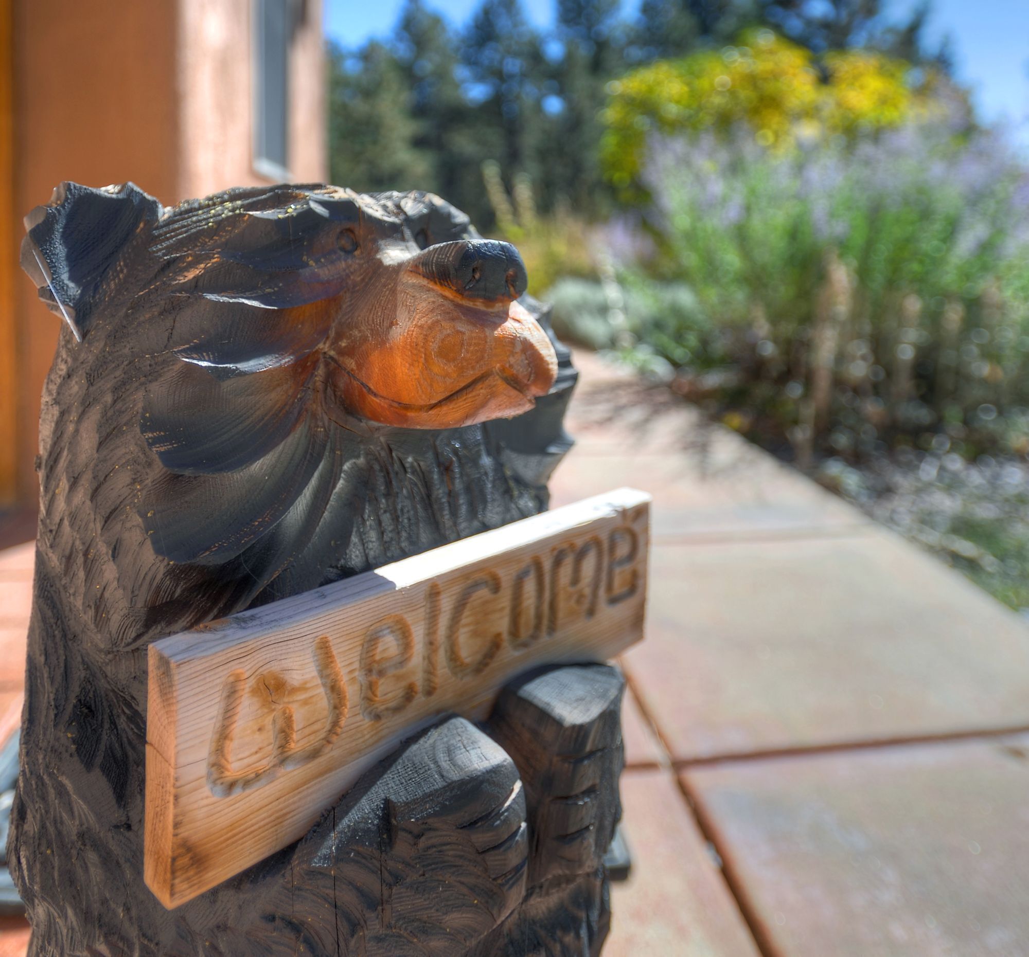 A wooden bear sculpture holding a sign that reads "Welcome".
