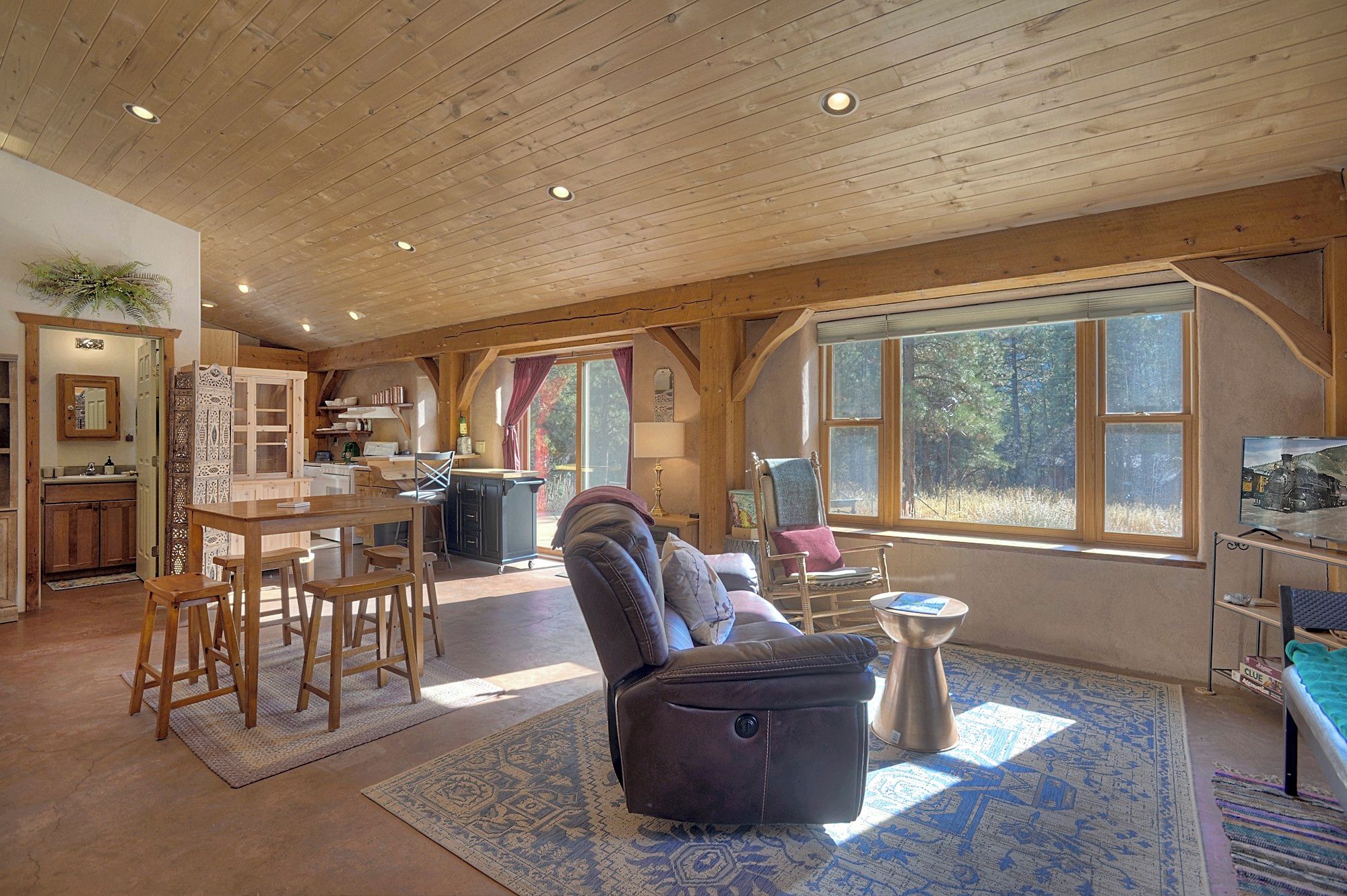Un salón amplio con un ventanal grande, un comedor con mobiliario de madera y una cocina con estanterías empotradas.