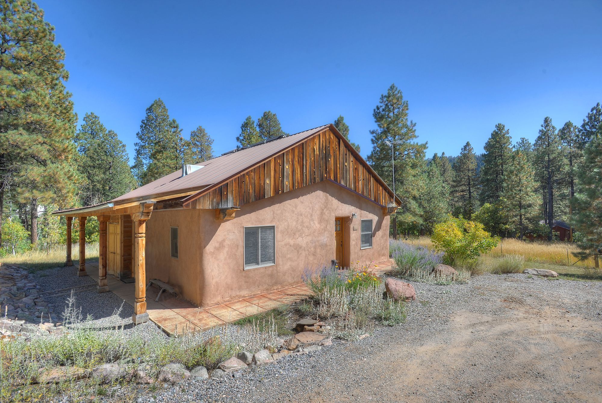 A rustic cabin with a wooden exterior, a porch, and a gravel driveway surrounded by trees.