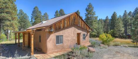 A rustic cabin with a wooden exterior, a porch, and a gravel driveway surrounded by trees.