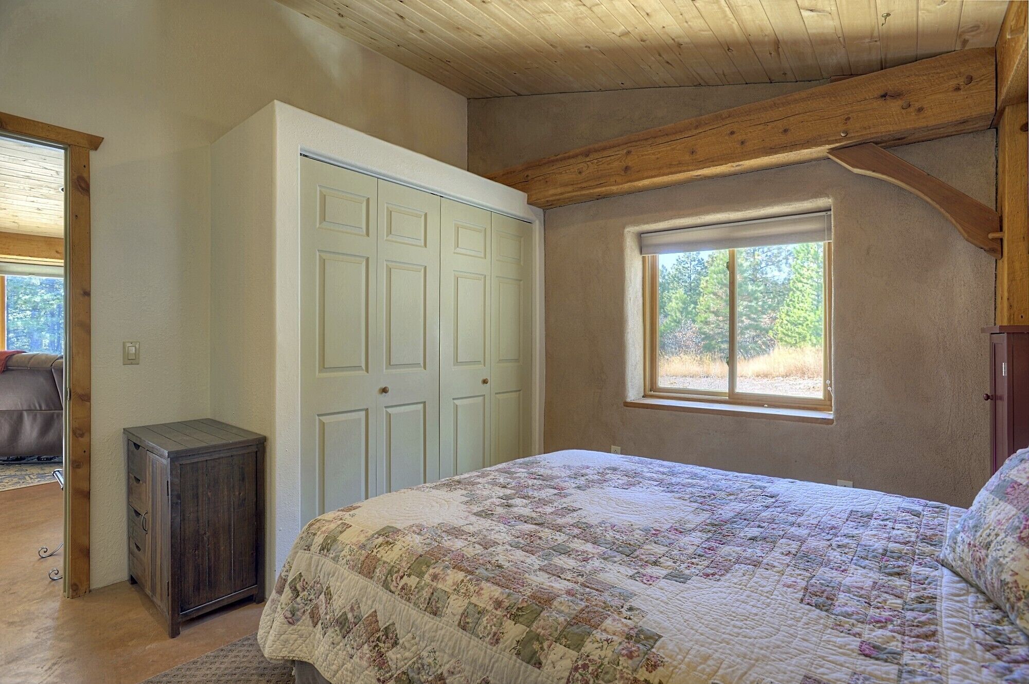 A bedroom with a bed, a wardrobe, a small cabinet, and a window with a view of trees.
