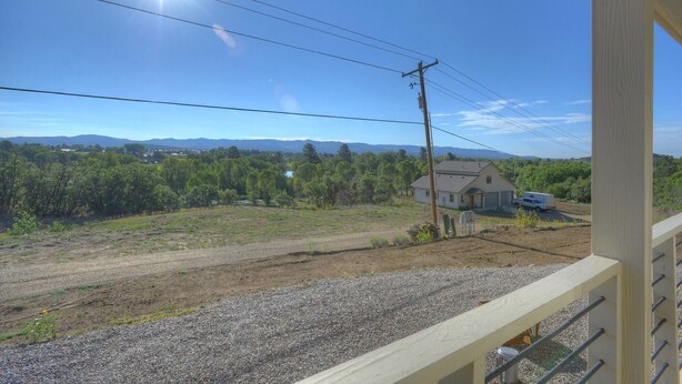 Une maison avec une allée gravillonnée, un véhicule garé et une vue sur une zone boisée avec des montagnes à l’horizon.