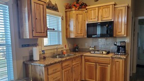 Una cocina con armarios de madera, un lavamanos de acero inoxidable, un microondas y una cafetera.