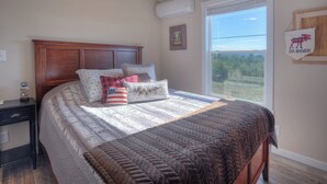 Un dormitorio con una cama grande, cabecera de madera, mesita de noche, ventana con vistas y aire acondicionado de pared.