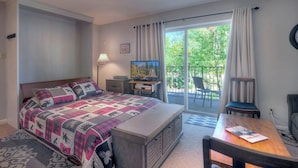 Une chambre avec un lit, une télévision, un bureau et un balcon équipé d’une chaise.