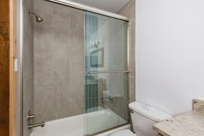 Une cabine de douche avec une porte en verre, une baignoire et des toilettes.