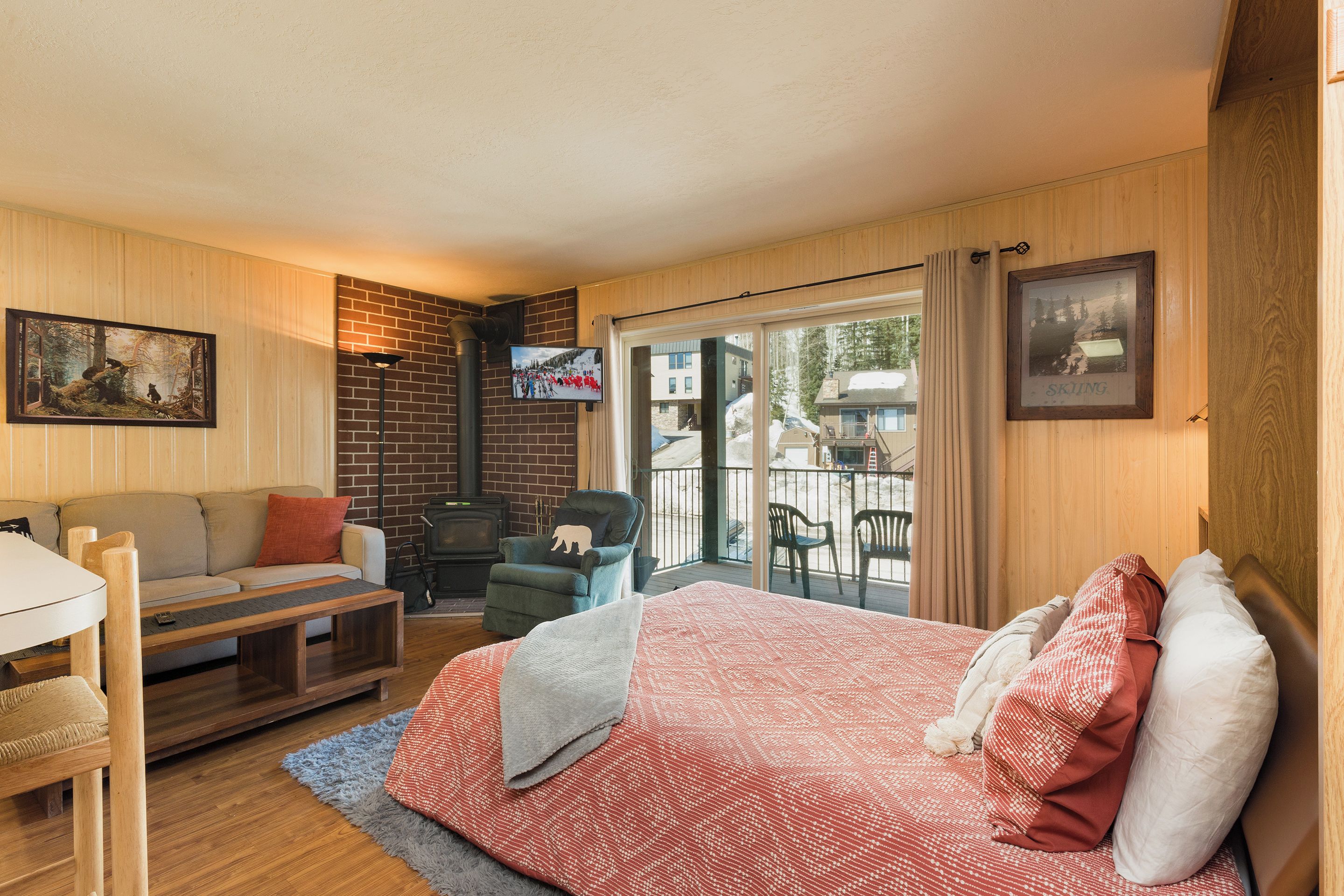A cozy room with a bed, a sofa, a TV, a fireplace, and a balcony with chairs.