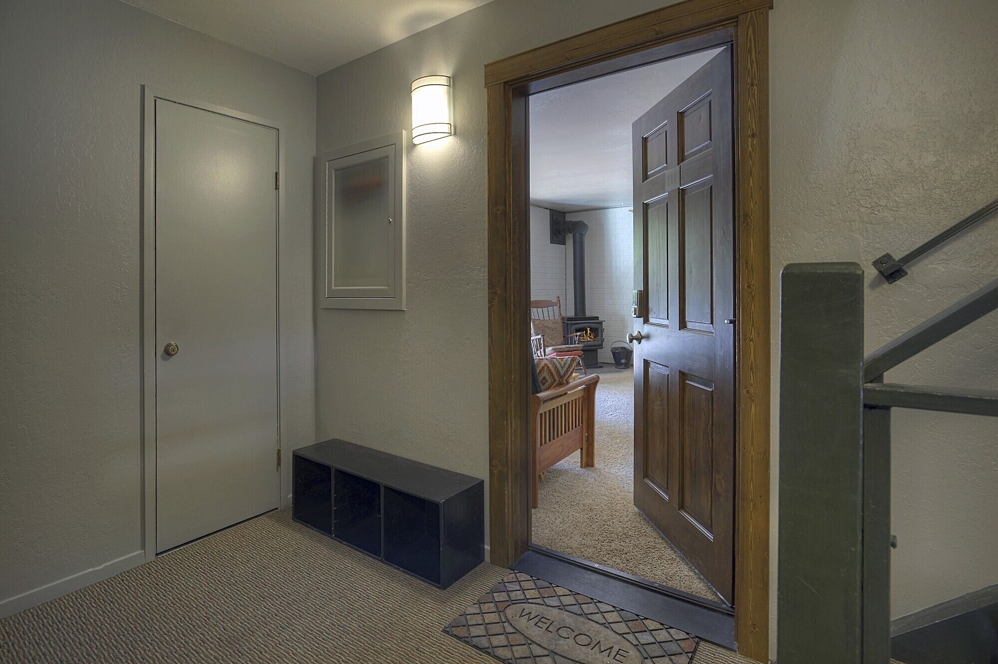 A hallway with a bench, a welcome mat, and a door leading to a room with a fireplace.