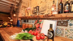 A kitchen counter with fresh vegetables, a bottle of olive oil, and wine bottles on a shelf.