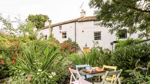 A garden with a table and chairs, surrounded by lush greenery and flowers.