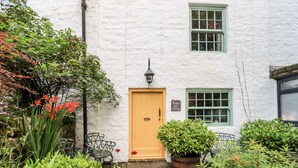 A white building with a yellow door, a sign reading "Bonny Bit's Cottage," and a stone pathway leading to a bench.