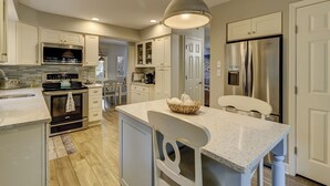 Una cocina moderna con armarios blancos, un refrigerador de acero inoxidable y una encimera de granito.