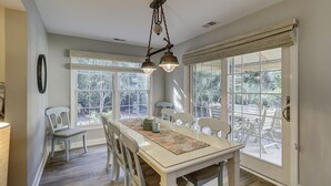Un comedor con mesa y sillas, ventanas amplias y una lámpara colgante.