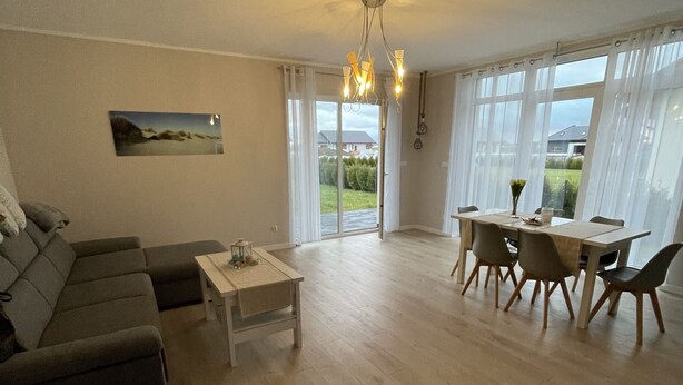 A spacious living room with a sofa, a dining table with chairs, and a view through large windows.